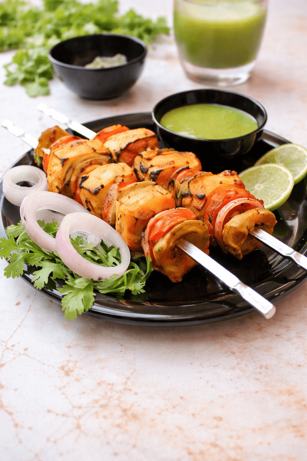 Paneer tikka skewers with grilled vegetables, served with green chutney, onion rings, and lime.