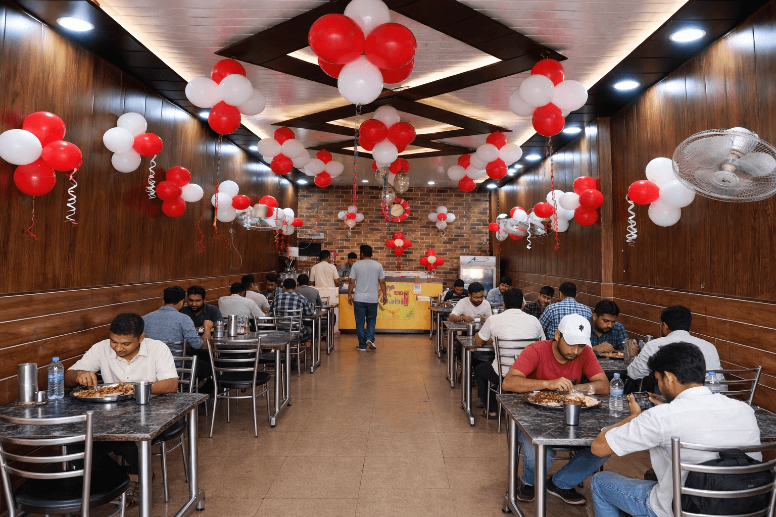 People eating at tables in a restaurant decorated with festive red and white balloons.