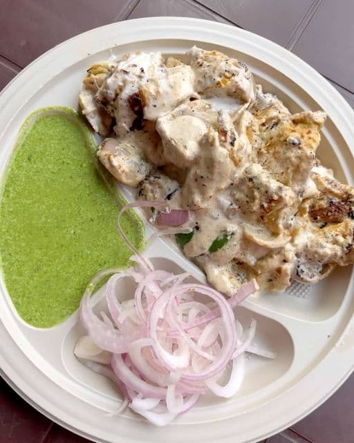 Creamy malai tikka with green chutney and sliced red onions on a white plate.