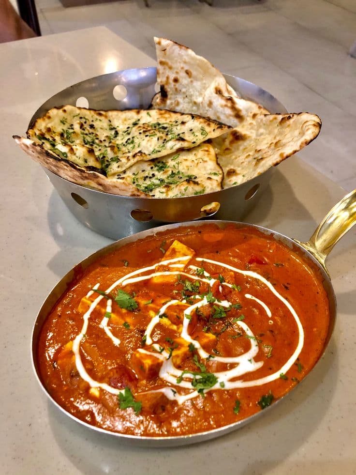 Creamy paneer curry in a metal pan served with a basket of fresh naan.