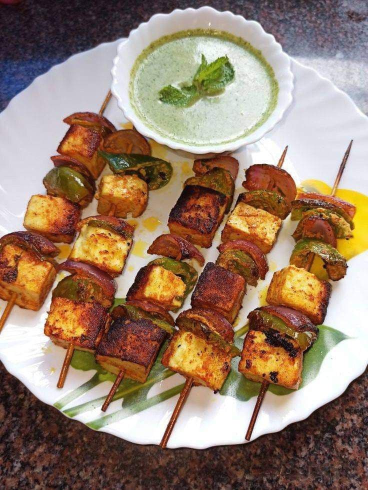 Grilled paneer tikka skewers with peppers and onions served with a bowl of mint chutney.