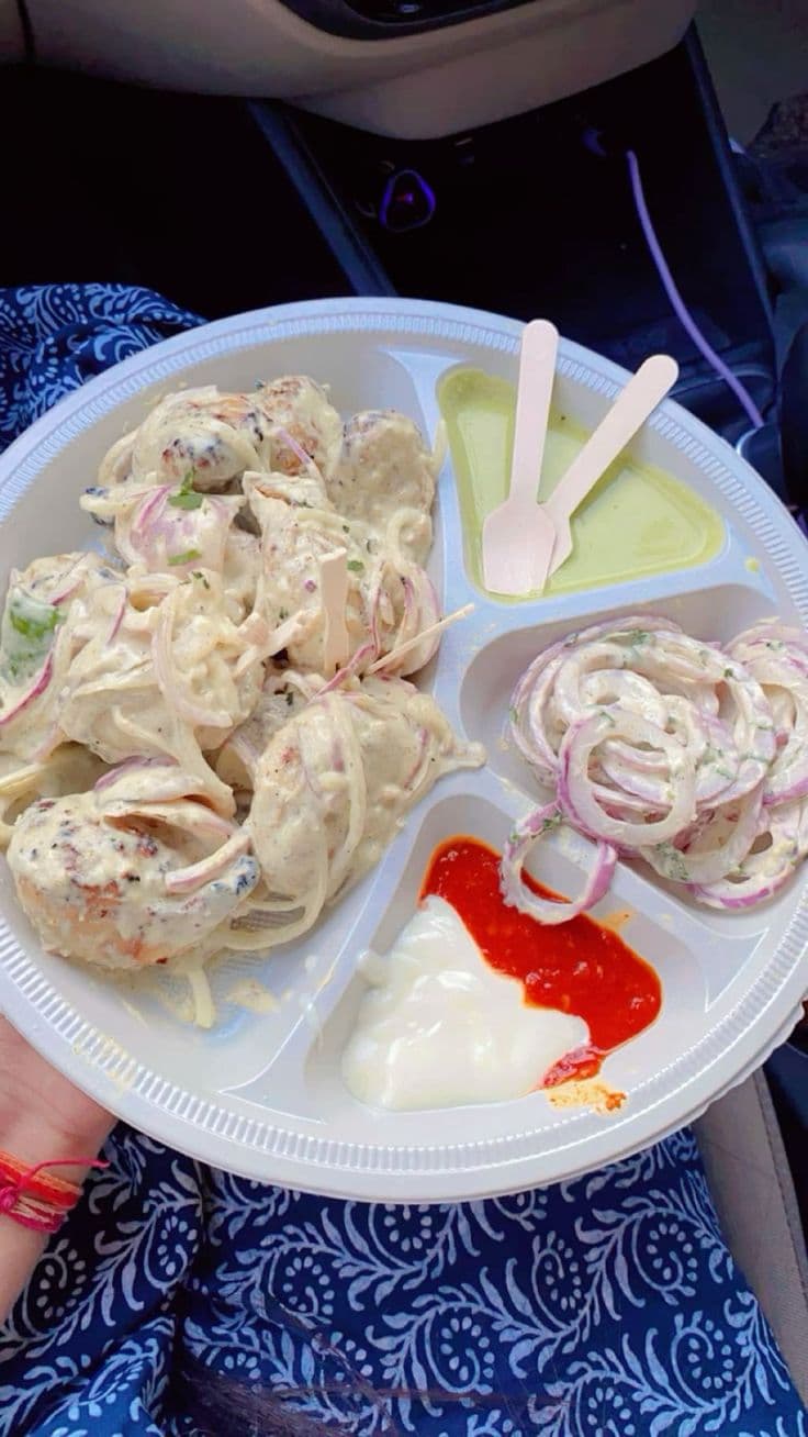 Creamy malai tikka with sliced onions, green chutney, and sauces on a white divided plate.